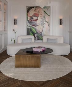 a living room with white couches and a painting on the wall behind it's glass coffee table