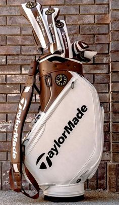 a golf bag with the words taylormade written on it, sitting in front of a brick wall