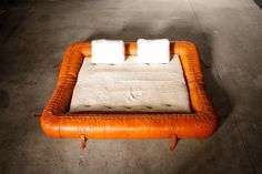 an orange leather ottoman with two white pillows on the top and one in the middle