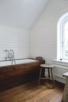 an old fashioned bathtub in a white bathroom next to a window with a wooden stool