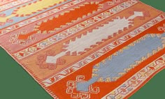 an orange, blue and yellow rug with designs on the bottom half is laying flat against a white background