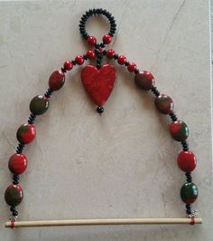 a beaded necklace with a red heart hanging from it's center, next to a wooden stick