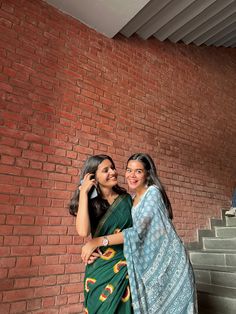 two women standing next to each other in front of a brick wall and staircases