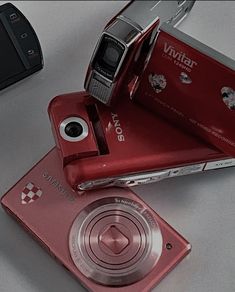 a red camera sitting on top of a table next to a cell phone