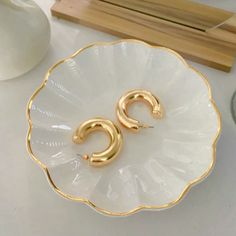 two gold hoop earrings sitting on top of a white plate next to a glass vase