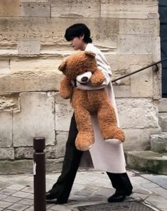 a woman walking down the street with a large teddy bear in her arms and holding onto a pole