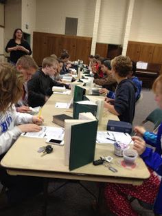 a group of kids sitting at a table with papers and pens