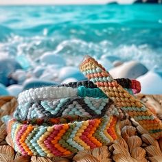 multicolored bracelets sitting on top of a woven basket next to the ocean