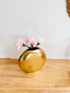 a gold vase with pink flowers in it on a wooden table next to a mirror