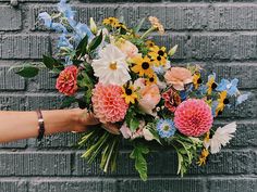 a person holding a bouquet of flowers in front of a brick wall with blue and pink flowers