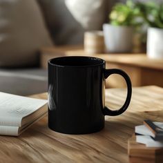 a black coffee mug sitting on top of a wooden table next to an open book