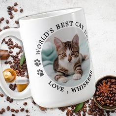 a white coffee mug with a cat on it and some coffee beans around the cup