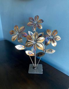 a metal flower sculpture sitting on top of a wooden table next to a blue wall