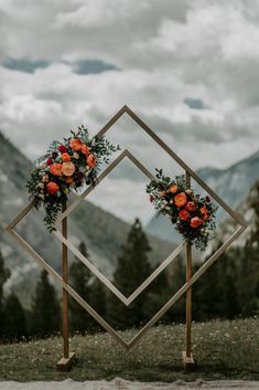 two square wooden stands with flowers and greenery on them in front of some mountains