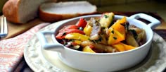 a white bowl filled with vegetables on top of a plate next to bread and knife