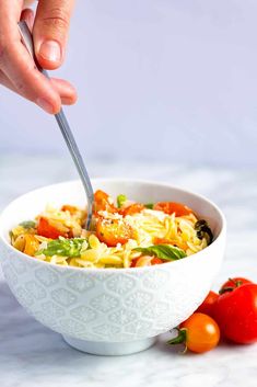 a person is holding a fork in a bowl of pasta with tomatoes on the side