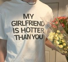 a man is holding flowers and wearing a t - shirt that says my girlfriend is hotter than you