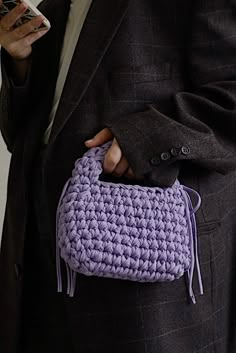 a person wearing a suit and holding a purple crochet purse in their hand