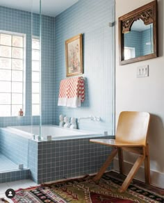 a blue tiled bathroom with a wooden chair and mirror above the bathtub, along with a rug on the floor