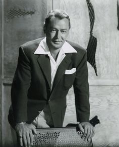 black and white photograph of man in suit leaning on an old suitcase with his hand on it