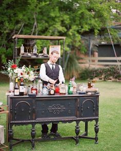 a man standing behind an old fashioned bar with bottles and glasses on the top shelf