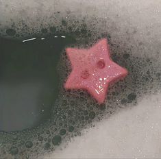 a pink star shaped object floating on top of some foamy water with bubbles around it