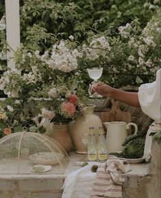 a woman sitting at a table with flowers and plants in vases next to her