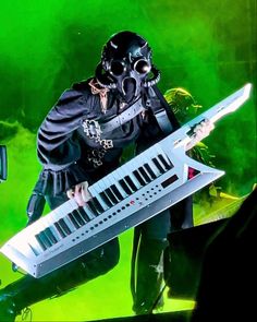 a man in a gas mask holding a keyboard and wearing a black outfit with chains on his neck