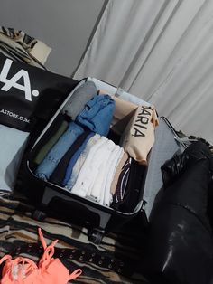 an open suitcase filled with clothes on top of a bed next to a pair of shoes