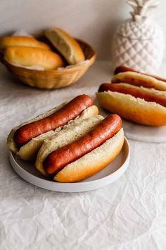 two hot dogs on buns and some bread in a bowl next to pineapple