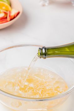 a bottle of wine being poured into a glass bowl filled with water and fruit salad