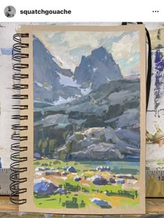 an open notebook with a painting of mountains in the background