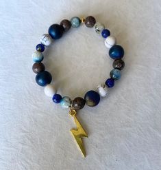 a bracelet with a gold lightning charm and blue agate, white marble beads on it