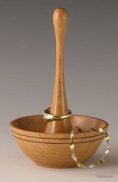 a wooden bowl with two gold rings on the bottom and a wood spoon in the middle