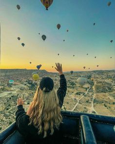 a woman in a hot air balloon looking out at the sky with many balloons flying above her