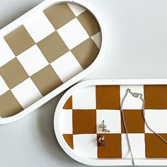 two trays with jewelry on them sitting next to each other, one has a checkerboard design