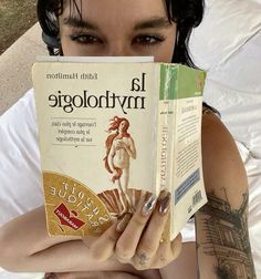 a woman is reading a book on her bed while holding it up to her face