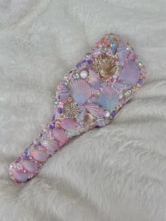 a pink and purple hair brush on a white fur covered surface with pearls, crystals and beads