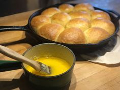 bread rolls in a pan and a bowl of orange liquid on a wooden cutting board