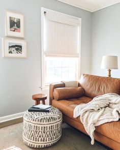 a living room with a brown leather couch and ottoman next to a window covered in blankets