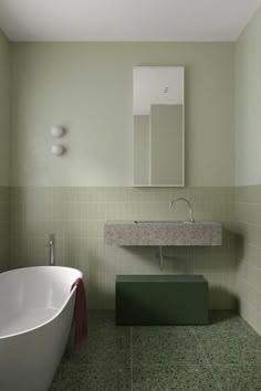 a bathroom with green tiles and a white bathtub next to a mirror on the wall