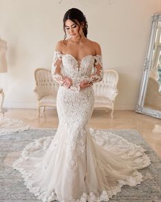 a woman in a white wedding dress standing on a rug with her arms behind her back