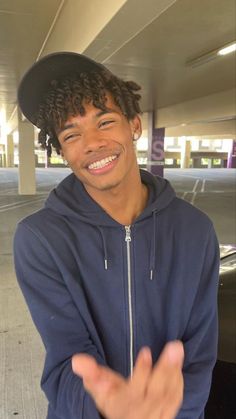 a young man with curly hair wearing a black hat