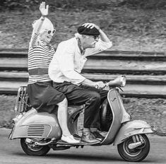 two people riding on the back of a scooter with their arms in the air