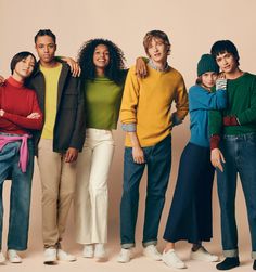 four people standing together in front of a beige background wearing sweaters and jeans with their arms around each other