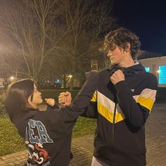 a young man and woman standing next to each other in front of a building at night