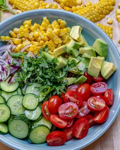 a blue bowl filled with lots of different types of vegetables next to corn on the cob