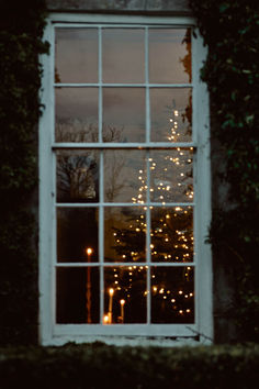 a window that has some lights in the windows sill and trees outside it at night