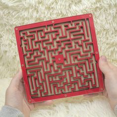 a person holding a red square shaped object with a maze design on the front in their hands