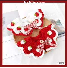 two red and white crocheted baby booties with bows on the side, sitting on top of a wooden plate